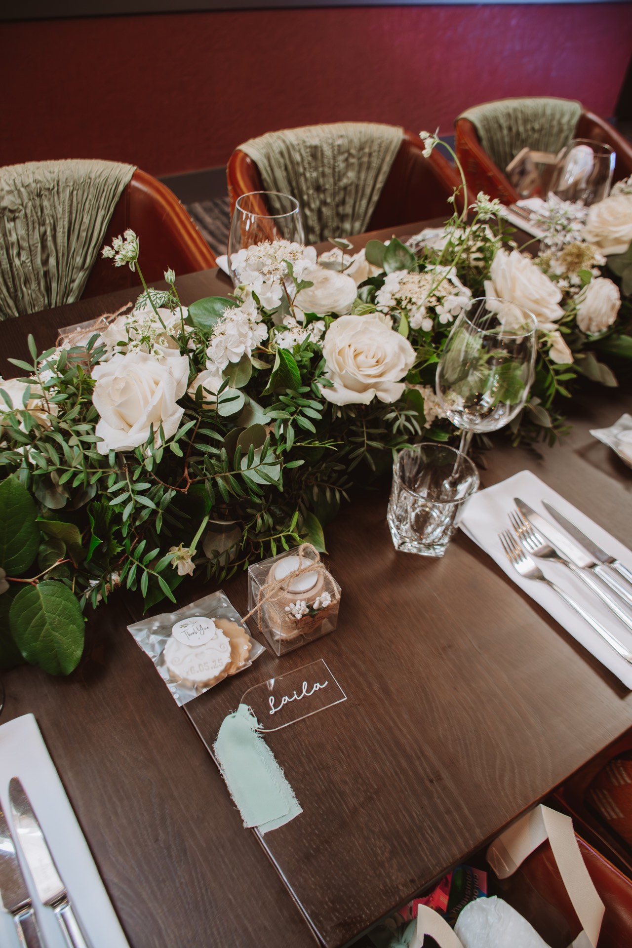 An elegant wedding table setting with white roses, greenery and personalised gifts