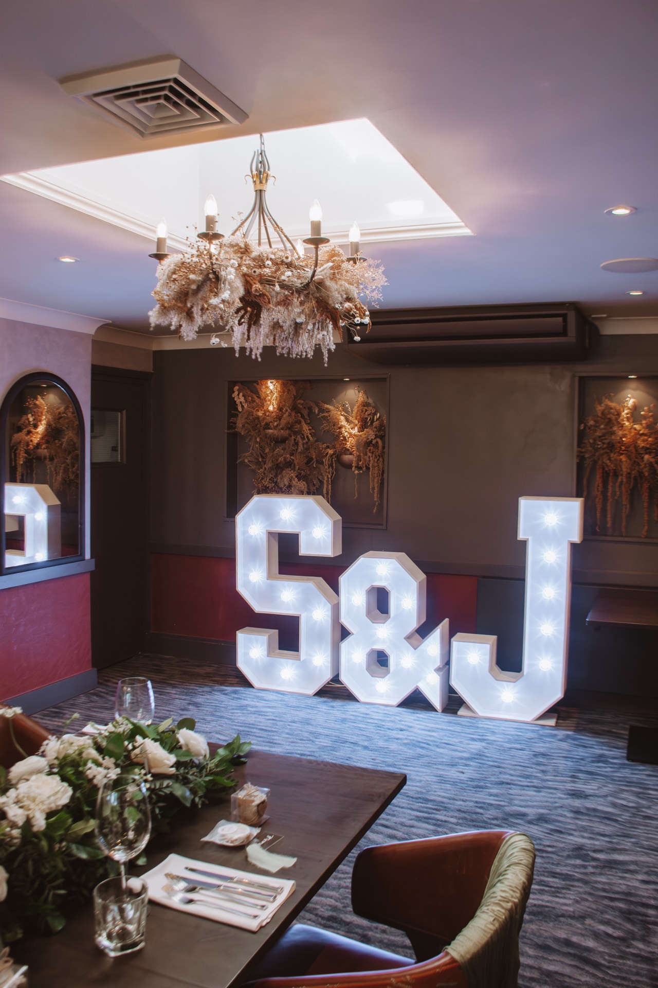 Illuminated large letters S and J in a decorated room with floral arrangements and a chandelier above